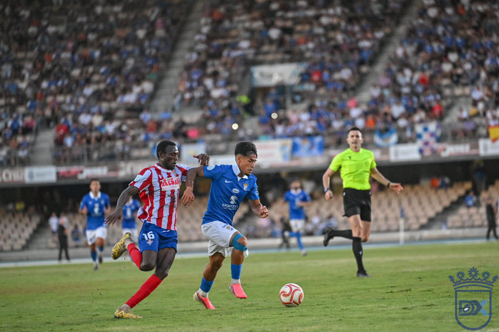 A Xerez CD player drives forward with the ball chased by a Don Benito opponent under the referee's gaze